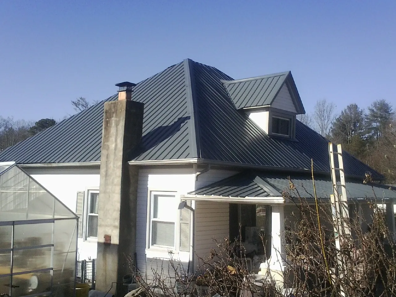 Dark blue standing seam metal roof on a white farmhouse with dormer — Slate & Tile Roof Repair by Roofing Brothers in Marion Station