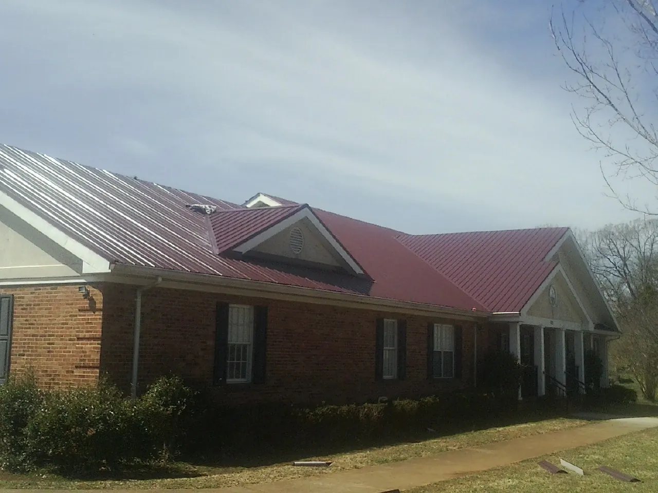 Red metal roof with gabled entries on a long brick building, from a Hail Damage Roof Repair job in Marion Station