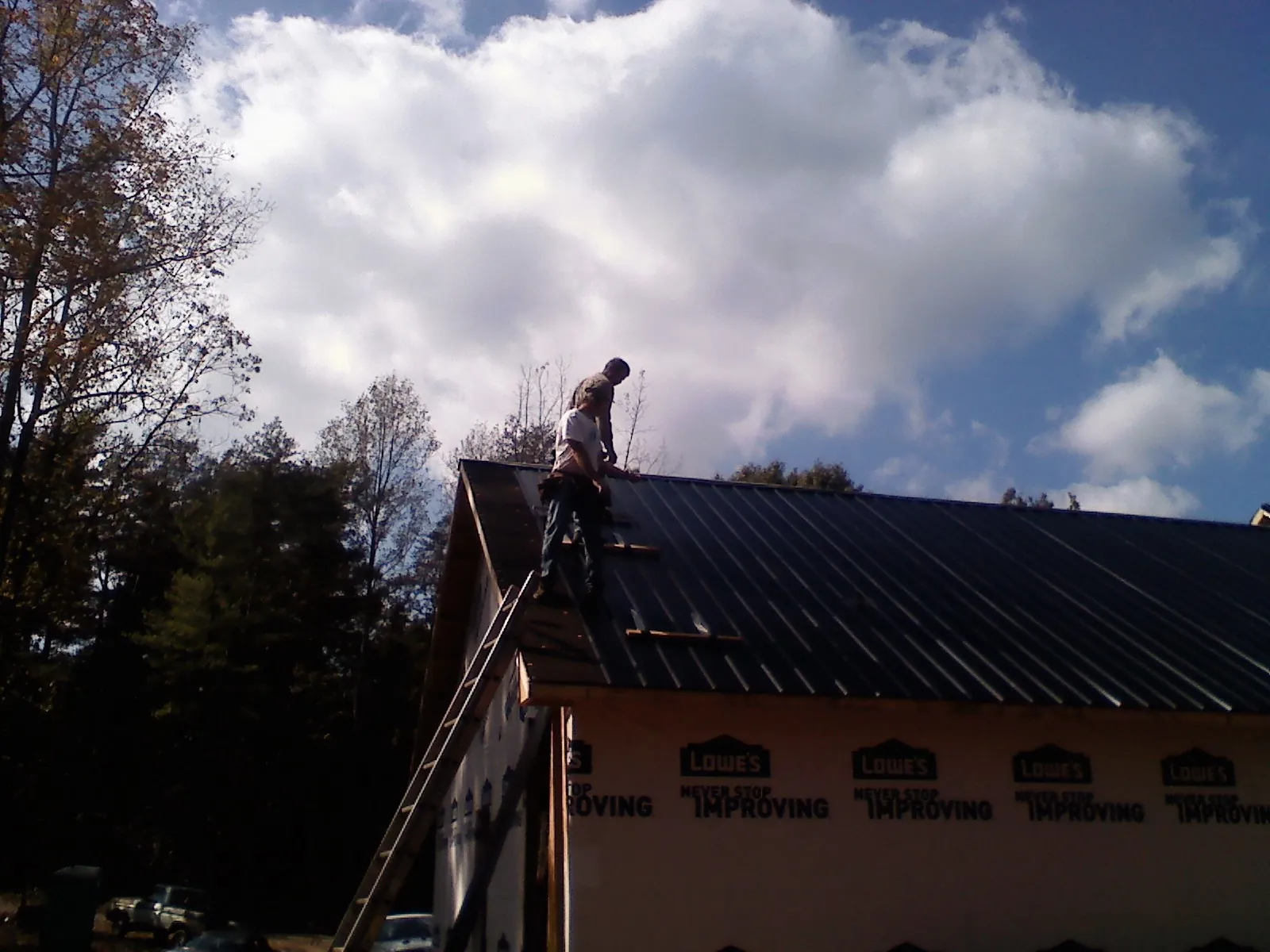 Roofer fastening dark metal panels high against a cloudy sky, from a Roof Inspection job in Marion Station