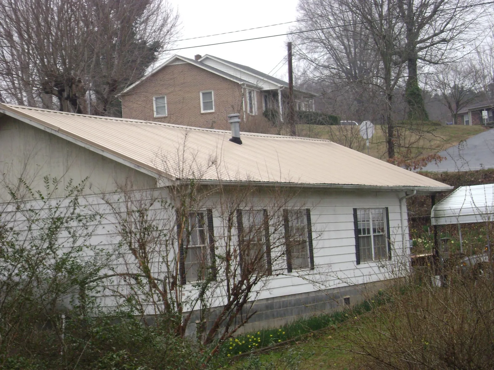 Tan metal roof on a white sided house set into a hillside — Commercial Roofing by Roofing Brothers in Marion Station